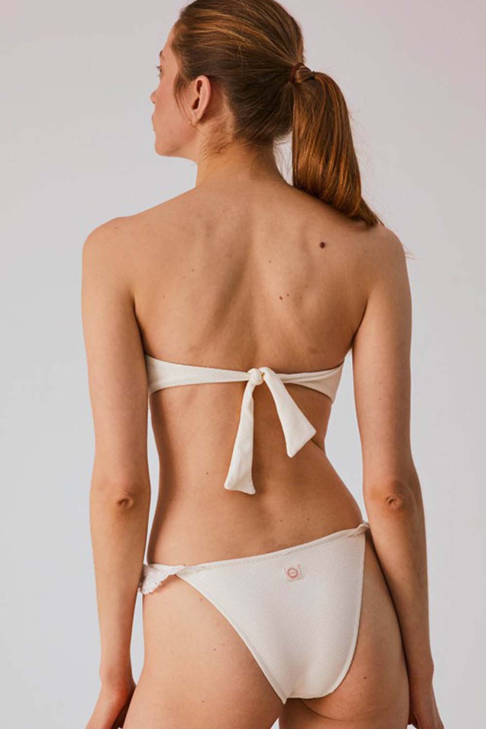 modelo de espalda con bikini color blanco crudo con detalles de volante corte semi brasileño 