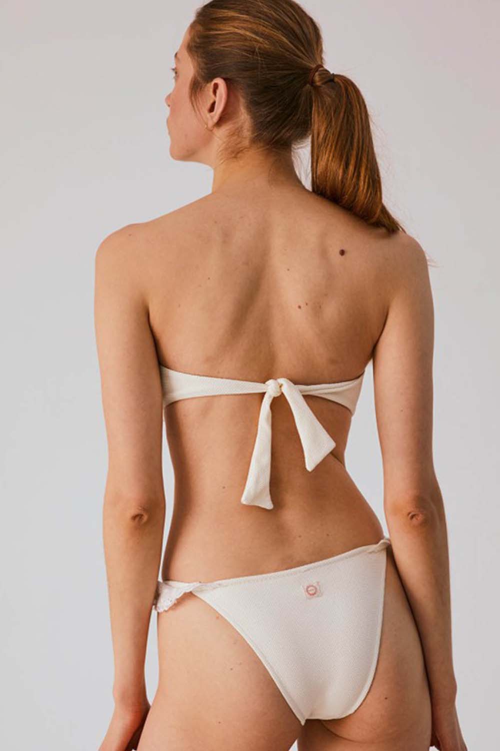 modelo de espalda con bikini color blanco crudo con detalles de volante corte semi brasileño
