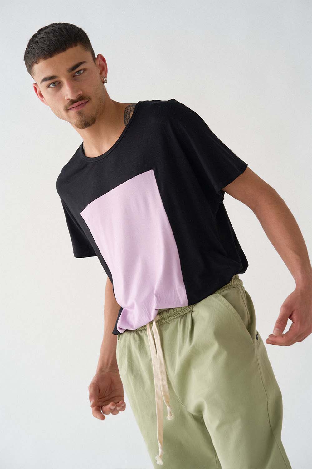 imagen de detalle de lado del modela con camiseta quadrilaterus negro y lila y pantalón worker verde