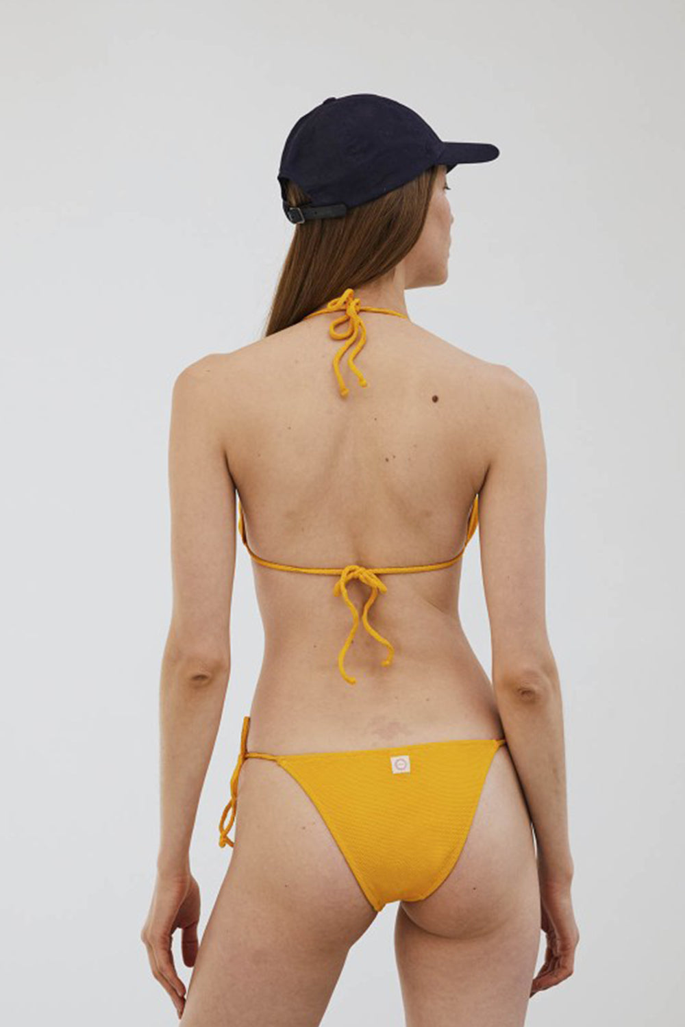chica de espalda con bikini amarillo con tiras, aros y nudos al lado de la braga y gorro azul marino